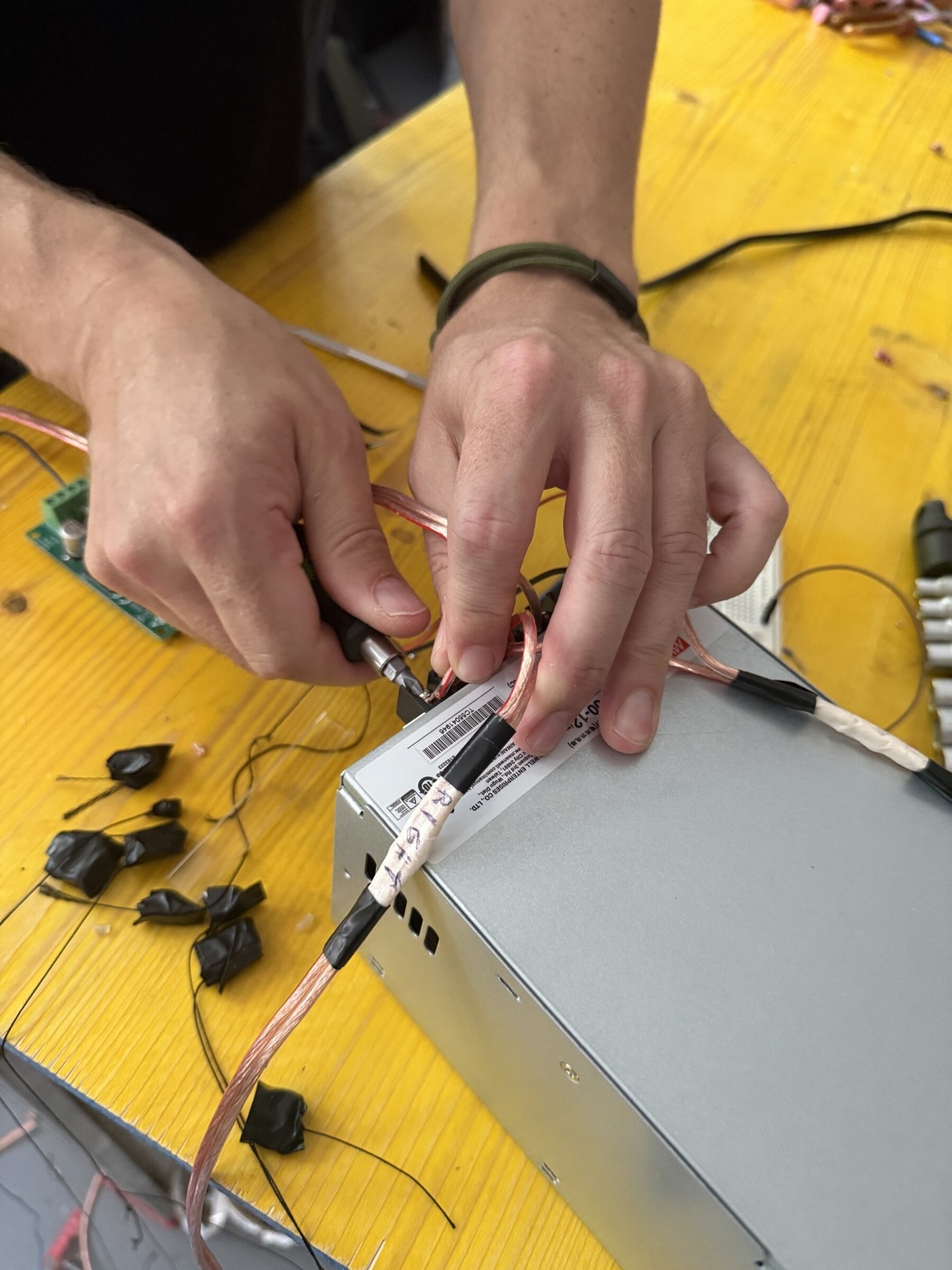 Zwei Hände arbeiten an der Elektronikbox, Litzen und Platine im Vordergrund